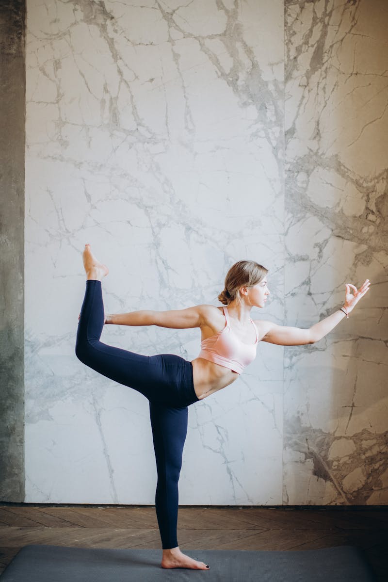 A woman performing a yoga pose indoors, showcasing flexibility and balance for wellbeing.
