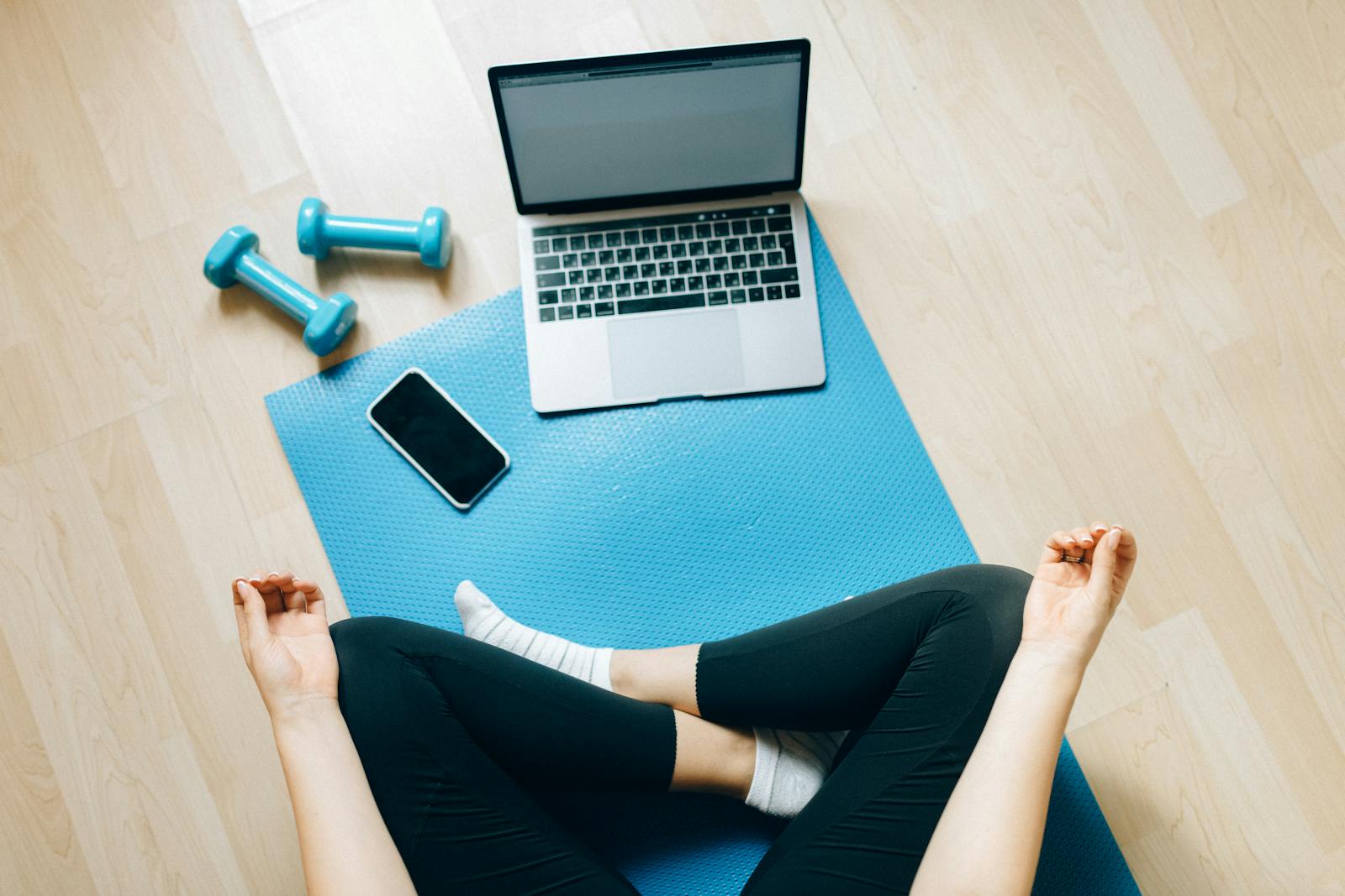 Yoga mat setup with laptop and dumbbells for home fitness.